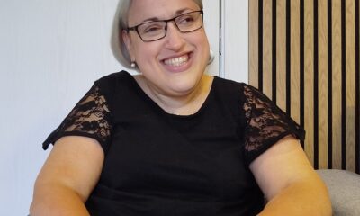 Na fotografiji se nalazi osoba koja sjedi u invalidskim kolicima i veselo se smiješi prema kameri. Ima kratku sijedu kosu, nosi naočale i odjevena je u crnu majicu s čipkastim rukavima. Na lijevom zapešću nosi narukvicu s privjescima. U pozadini se vidi bijela vrata i zid obložen drvenim panelima. Atmosfera fotografije djeluje toplo i prijateljski.