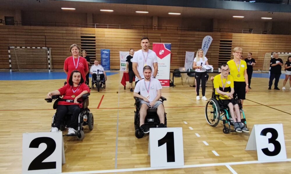 Fotografija prikazuje tri osobe u invalidskim kolicima koje stoje iza brojeva mjesta koje su osvojili na soirtskom natjecanju. Isto tako, na vratu imaju i medalje koje su osvojili.