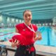 Fotografija prikazuje djevojku koja ima srebrnu medalju oko vrata, a u ruci drži neku igračku, dok se iza nje nalzi bazen.