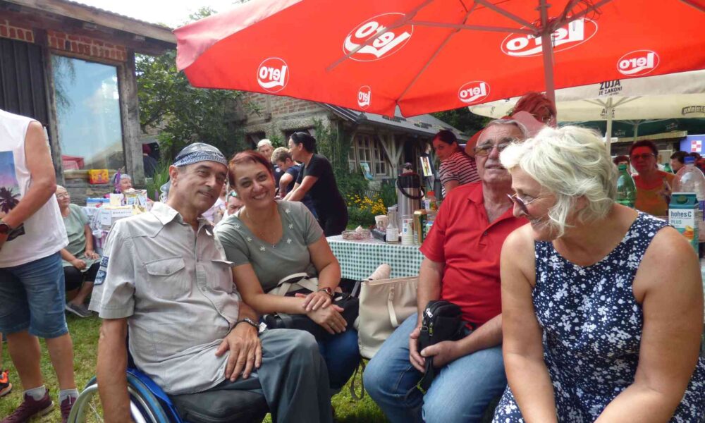 Fotografija prikazuje nekoliko ljudi u invalidskim kolicima pod suncobranom.