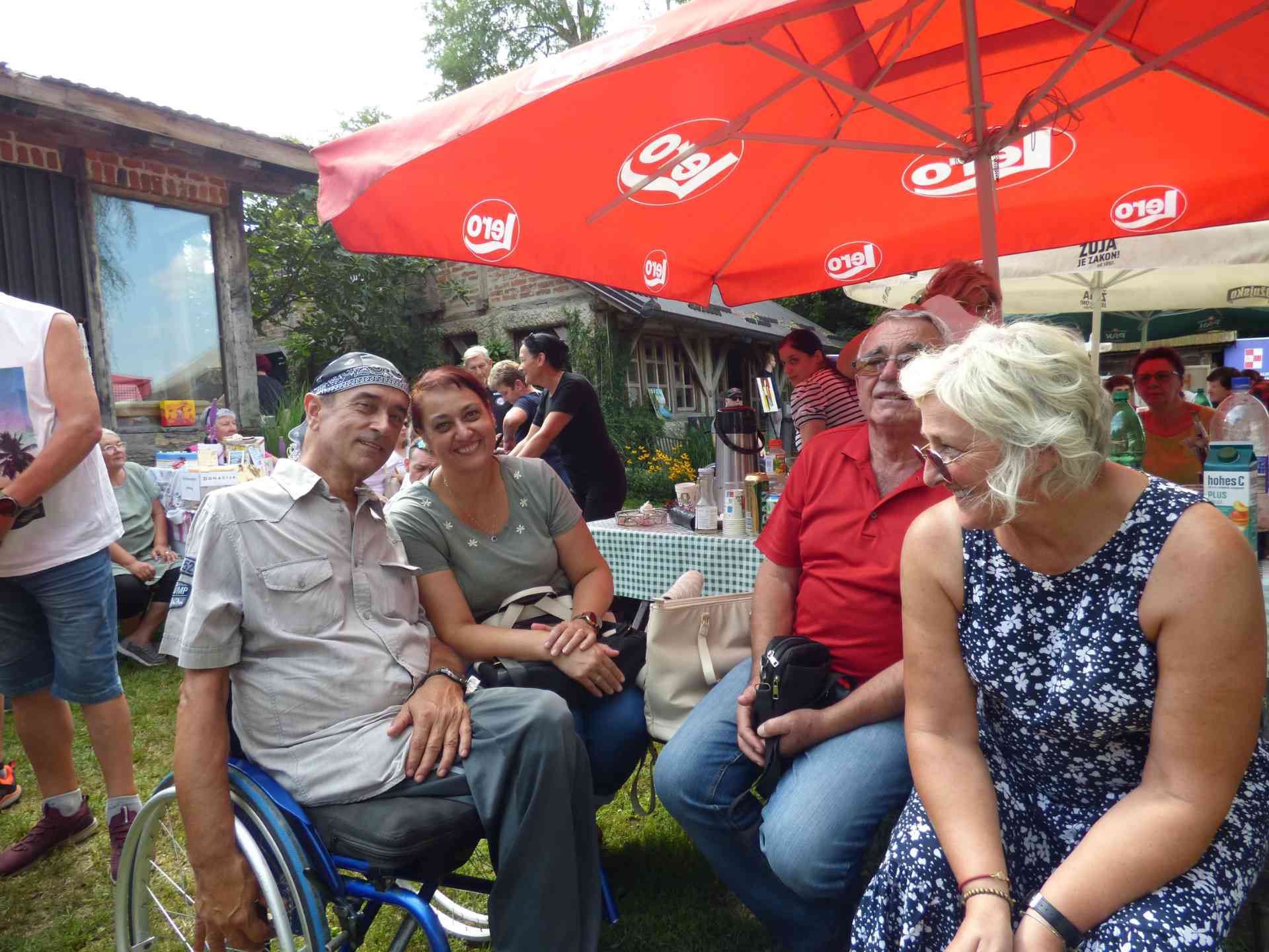 Fotografija prikazuje nekoliko ljudi u invalidskim kolicima pod suncobranom.