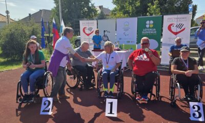Fotografija prikazuje nekoliko ljudi u kolicima koji se nalaze na atletskoj stazi. Ispred njih nalaze se brojevi koji označavaju na kojem je mjestu tko završio. Neki od njih drže medalje u rukama.