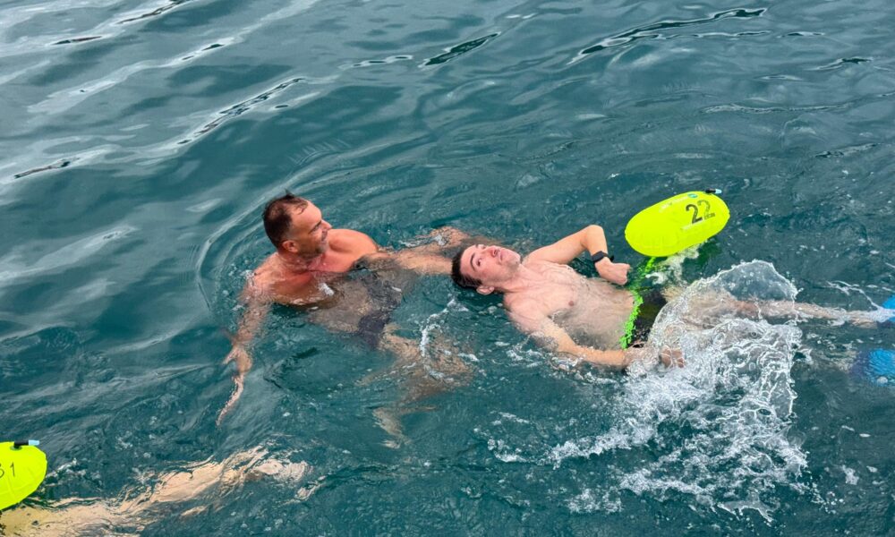Fotografija prikazuje osobu s invaliditetom kako zajedno s još jednim čovjekom pliva u moru.