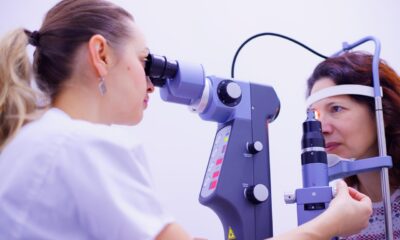 Na fotografiji se prikazuje oftalmološki pregled oka koji provodi zdravstveni djelatnik pomoću biomikroskopa s prorezom (slit lamp). Liječnik pažljivo promatra pacijentovo oko kroz uređaj, koji je opremljen raznim kontrolnim tipkama i kotačićima za podešavanje. Pacijentica sjedi s bradom i čelom oslonjenima na posebne potpornje kako bi glava ostala stabilna tijekom pregleda. Ova scena prikazuje uobičajeni, ali vrlo važan postupak u oftalmologiji, koji omogućuje detaljan pregled prednjeg i stražnjeg segmenta oka. Takvi pregledi pomažu u dijagnosticiranju raznih očnih bolesti i stanja, poput glaukoma, upala, oštećenja rožnice ili mrežnice.