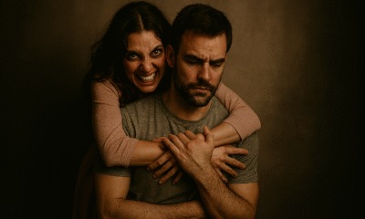 Fotografija prikazuje par u dramatičnom, emocionalno nabijenom zagrljaju. Žena stoji iza muškarca, obavijajući ga rukama oko prsa, dok on sjedi ukočeno, s rukama prekriženim preko vlastitog tijela. Fotografija snažno dočarava dinamiku opsesivne ljubavi—mješavinu privrženosti, kontrole i nelagode. Ženin izraz sugerira intenzivnu potrebu za blizinom, dok muškarčev stav odaje otpor i unutarnji konflikt.