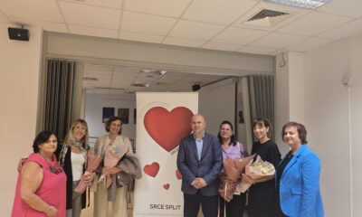 Na fotografiji je sedam odraslih osoba koje stoje u zatvorenom prostoru ispred bannera s velikim crvenim srcem i tekstom udruge "Srce Split – Udruga osoba sa cerebralnom paralizom". Osobe su odjevene svečano ili polusvečano, a tri od njih drže bukete cvijeća, što sugerira da su možda nagrađeni, zahvaljeni ili posebno istaknuti u sklopu događaja.