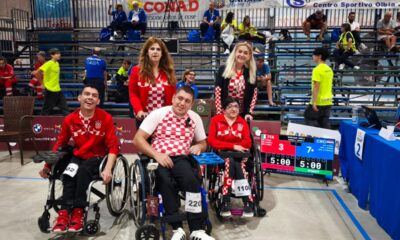 Slika prikazuje nekoliko ljudi na boccia terenu od kojih je troje u kolicima. Svi su obučeni u crvena hrvatska obilježja.