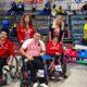 Slika prikazuje nekoliko ljudi na boccia terenu od kojih je troje u kolicima. Svi su obučeni u crvena hrvatska obilježja.
