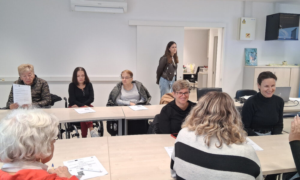 Sudionice edukacije sjede za stolovima s radnim materijalima tijekom predstavljanja aplikacije Danova Next u prostorijama s EU obilježjima.