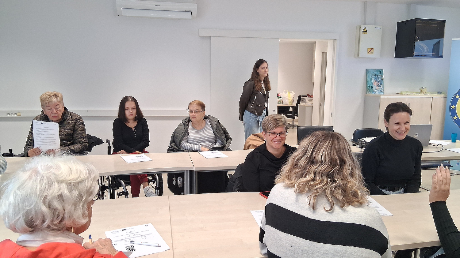 Sudionice edukacije sjede za stolovima s radnim materijalima tijekom predstavljanja aplikacije Danova Next u prostorijama s EU obilježjima.