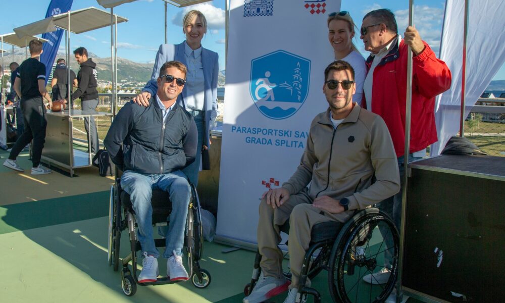 Fotografija prikazuje dva čovjeka u invalidskim kolicima, dok iza njih stoji troje ljudi te se nsalazi baner na kojem piše 'Parasportski savez grada Splita'.