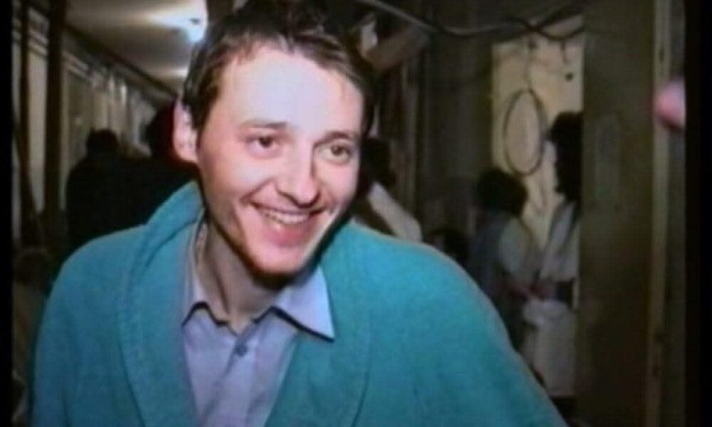 Na fotografiji je čovjek u zelenom džemperu i košulji koji se smije.