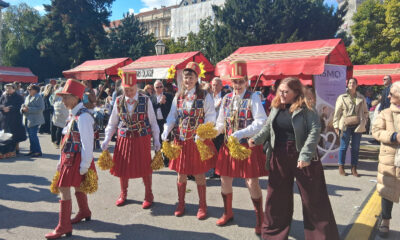 Skupina žena u šarenim kostimima i crvenim čizmama pleše na otvorenom tijekom manifestacije, okružena publikom.