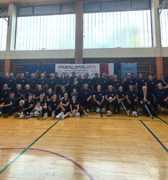 Velika skupina sudionika u sportskim majicama pozira u dvorani s košarkaškim koševima ispod transparenta „Prijateljstvo 2025“, s loptama za odbojku ispred sebe.