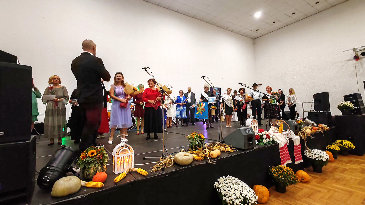 Sudionici i organizatori stoje na pozornici ukrašenoj jesenskim plodovima i cvijećem tijekom svečanog proglašenja izbora za Najbolju baku i djeda 2025. godine.