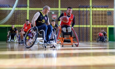 Fotografija prikazuje utakmicu košarke u kolicima. Jedan čovjek vodi loptu, dok protivnik stoji pokraj njega.