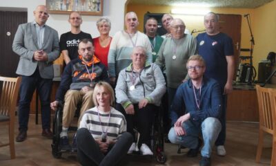 Fotografija prikazuje nekoliko ljudi kako stoje u zatvorenom prostoru. Neki od njih imaju medalje oko vrata, a jedna osoba je u invalidskim kolicima.