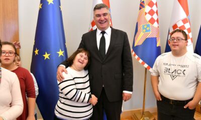 Na fotografiji je čovjek u odjelu koji krli djevojčicu sa Down Sindromom, a oko njega su i druga djeca s Down sindromom. Iza njih je nekoliko zastava, a između ostalog hrvatska zastava i zastava Europske Unije.
