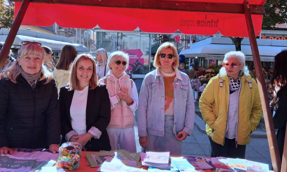 Skupina žena stoji iza štanda prekrivenog informativnim materijalima i promotivnim letcima tijekom obilježavanja Nacionalnog tjedna dojenja.
