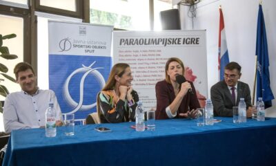 Fotografija prikazuje četvero ljudi za solom koji nešto pričaju. Jedna osoba drži mikrofon, a drugi je pozorno slušaju. Iza njih nalaze se baneri na kojima nešto piše i zastave Hrvatske i Europske unije.