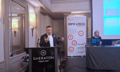Muškarac govori na konferenciji u hotelu Sheraton Zagreb, pored njega projekcija i plakat s informacijama HZJZ-ove info linije o ovisnostima.
