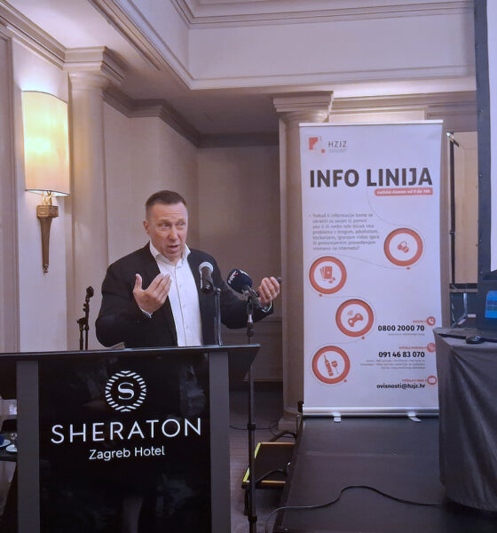Muškarac govori na konferenciji u hotelu Sheraton Zagreb, pored njega projekcija i plakat s informacijama HZJZ-ove info linije o ovisnostima.