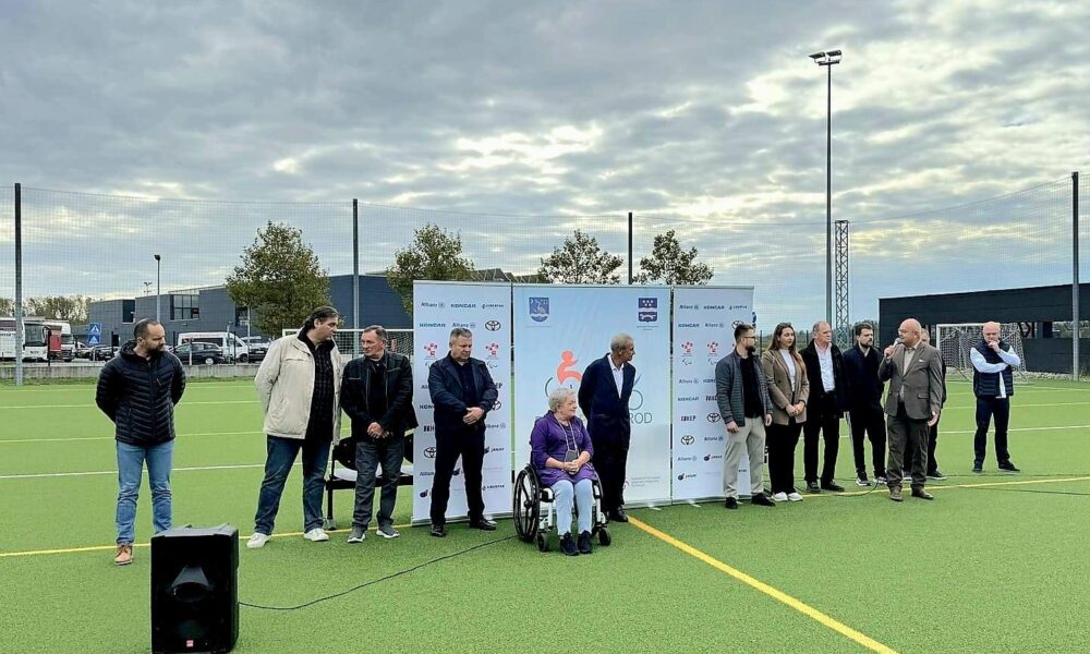 Fotografija prikazuje nekoliko ljudi lijepoi obučenih na sportskom igralištu. Jedna osoba je u invalidskim kolicima, dok drugi stoje.