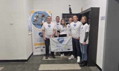 Fotografija prikazuje šest ljudi u bijelim majicama koji drže baner u rukama na kojem piše '#BeInclusiveWaterPolo'.