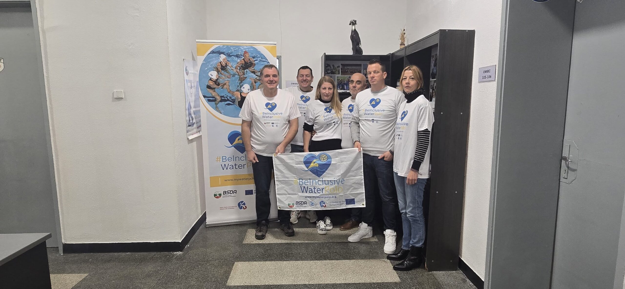 Fotografija prikazuje šest ljudi u bijelim majicama koji drže baner u rukama na kojem piše '#BeInclusiveWaterPolo'.