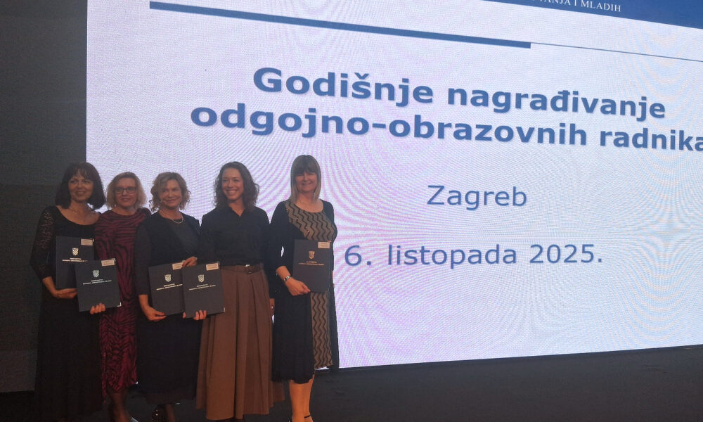 Pet žena stoji na pozornici s priznanjima u rukama ispred velikog ekrana s natpisom „Godišnje nagrađivanje odgojno-obrazovnih radnika, Zagreb, 6. listopada 2025.“