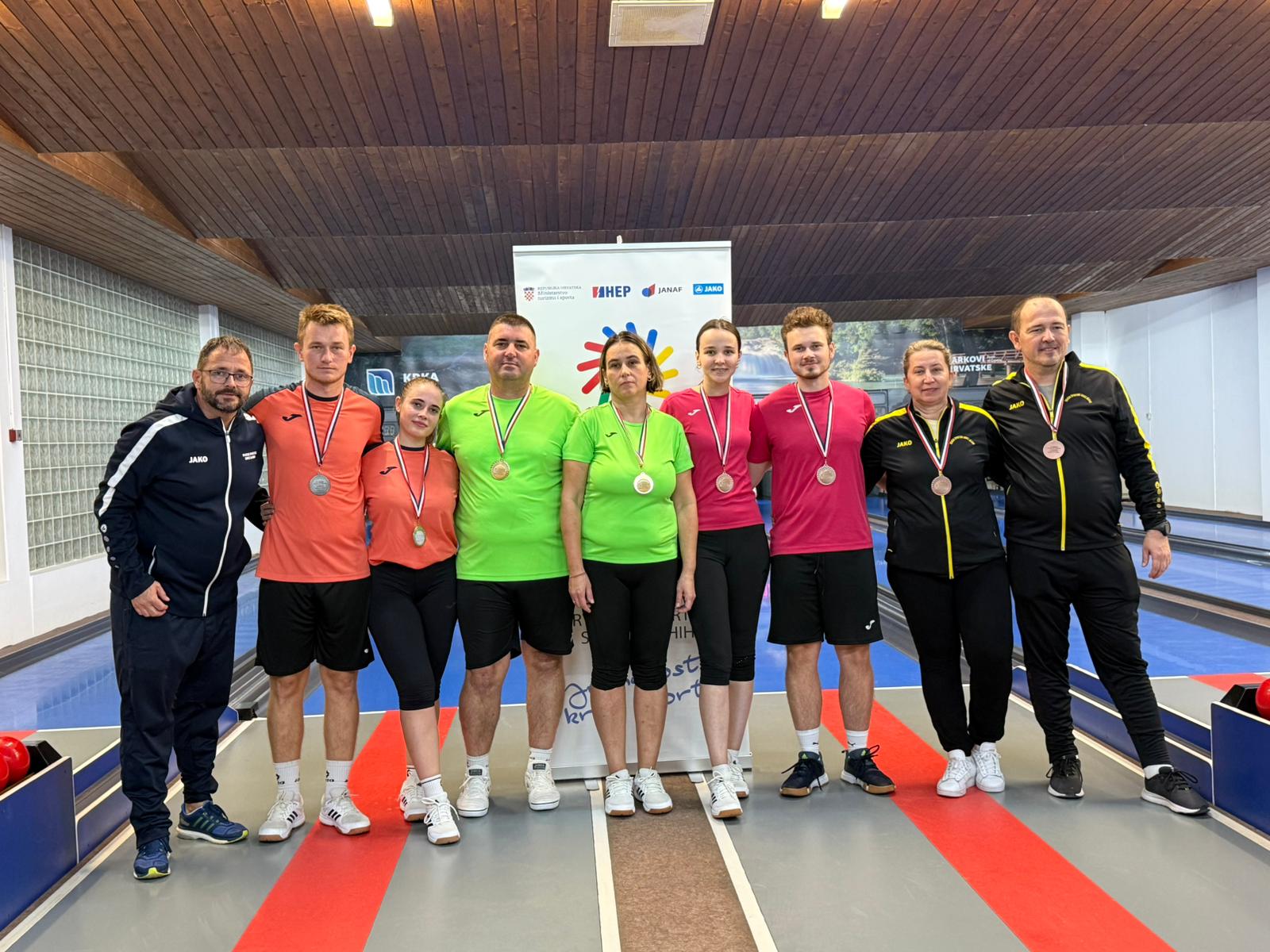 Fotografija prikazuje nekoliko ljudi s medaljama oko vrata na kuglani.