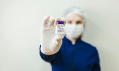 Na fotografiji se nalazi osoba u zaštitnoj medicinskoj odjeći koja nosi bijelu kiruršku masku i rukavice. Osoba drži u ruci malu bočicu botoxa s ljubičastim čepom, koju pokazuje prema kameri. Pozadina je jednostavna i svijetla, što dodatno naglašava bočicu u prvom planu. Fokus fotografije je na proizvodu, dok je lice osobe zamućeno, čime se stvara dojam profesionalnosti i čistoće medicinskog okruženja. Cjelokupni dojam slike sugerira kliničku preciznost i sigurnost u primjeni botoxa.