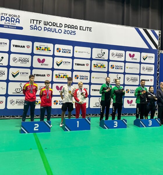 Fotografija prikazuje osmero ljudi kako stoje na postoljima s medaljama oko vrata. Iza njih je bilbord s natjecanja.