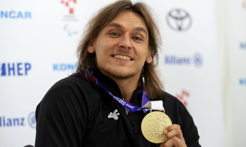 Na fotografiji je čovjek u invalidskim kolicima koji ima zlatnu medalju oko vrata i drži ju u rukama.