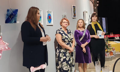 Četiri žene stoje uz izložene radove od stakla na zidu galerije, dok jedna od njih drži govor prilikom otvorenja izložbe.