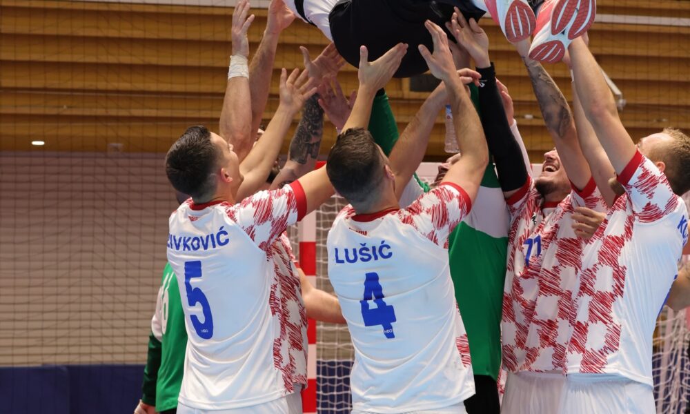 Fotografija prikazuje igrače u bijelom dresu sa crvenim kockicama kako bacaju čovjeka u zrak.