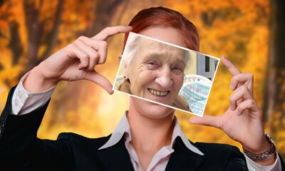 Na fotografiji je prikazana osoba u svečanom odijelu koja drži fotografiju ispred svog lica. Na toj fotografiji nalazi se starija osoba s osmijehom, a položaj slike je takav da prekriva lice osobe koja je drži, stvarajući dojmljiv vizualni efekt zamjene identiteta. Pozadina prikazuje šumski prizor u jesenjem ruhu – krošnje su obojene toplim nijansama narančaste, žute i smeđe, što stvara ugodnu i nostalgičnu atmosferu. Ova kompozicija snažno evocira teme prolaznosti vremena, transformacije i osobnog identiteta. Kontrast između mladenačkog tijela i starijeg lica na fotografiji može simbolizirati životni ciklus, sjećanja ili unutarnje stanje osobe. Topli tonovi prirode u pozadini dodatno pojačavaju emocionalni dojam – nježnost, prihvaćanje i kontemplaciju.