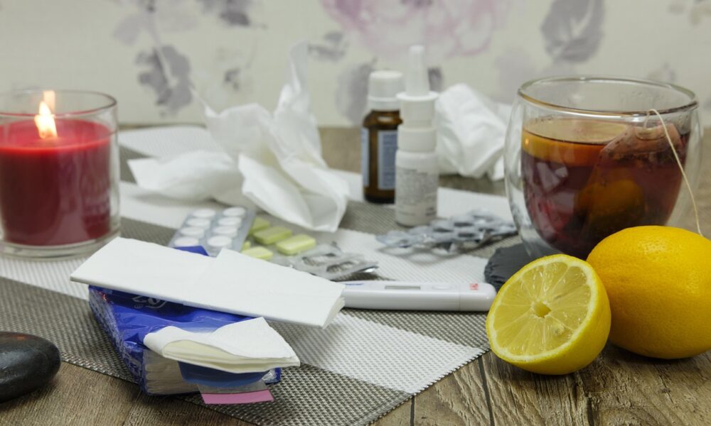 Na fotografiji se vidi stol prepun stvari koje se obično koriste kod prehlade ili gripe – pravi mali kutak za oporavak kod kuće.