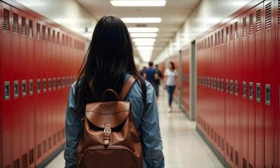 Na fotografiji se nalazi osoba s dugom tamnom kosom, obučena u traper jaknu i smeđi kožni ruksak, kako hoda niz školski hodnik. Perspektiva je snimljena s leđa, fokusirajući se na ruksak i simetrične redove crvenih ormarića koji se protežu s obje strane hodnika. Prostor je jako osvijetljen fluorescentnim svjetlima na stropu, a u pozadini se vide druge osobe koje hodaju ili stoje. Cijela scena odiše atmosferom svakodnevice u školskom okruženju, prizivajući teme obrazovanja, rutine i života učenika.
