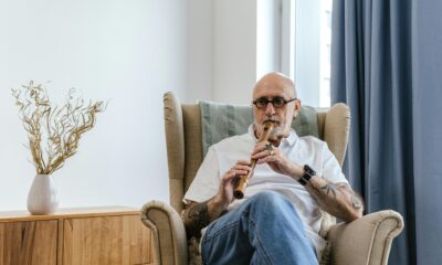 Fotografija prikazuje starijeg čovjeka kako sjedi na fotelji i svira flautu.