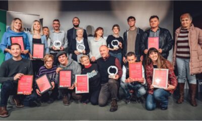 Na fotografiji se nalazi grupa od 17 osoba koje poziraju zajedno u zatvorenom prostoru, najvjerojatnije na pozornici ili u dvorani tijekom svečanosti dodjele nagrada. Većina sudionika drži crvene certifikate i okrugle trofeje, što upućuje na to da su primili priznanja za svoja postignuća. Atmosfera je svečana i vesela — svi izgledaju ponosno i zadovoljno.