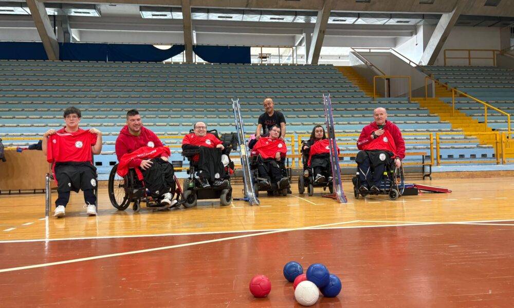 Fotografija prikazuje nekoliko ljudi u invalidskim kolicima koji su obučeni u crvene dresove, kako igraju bocciu.