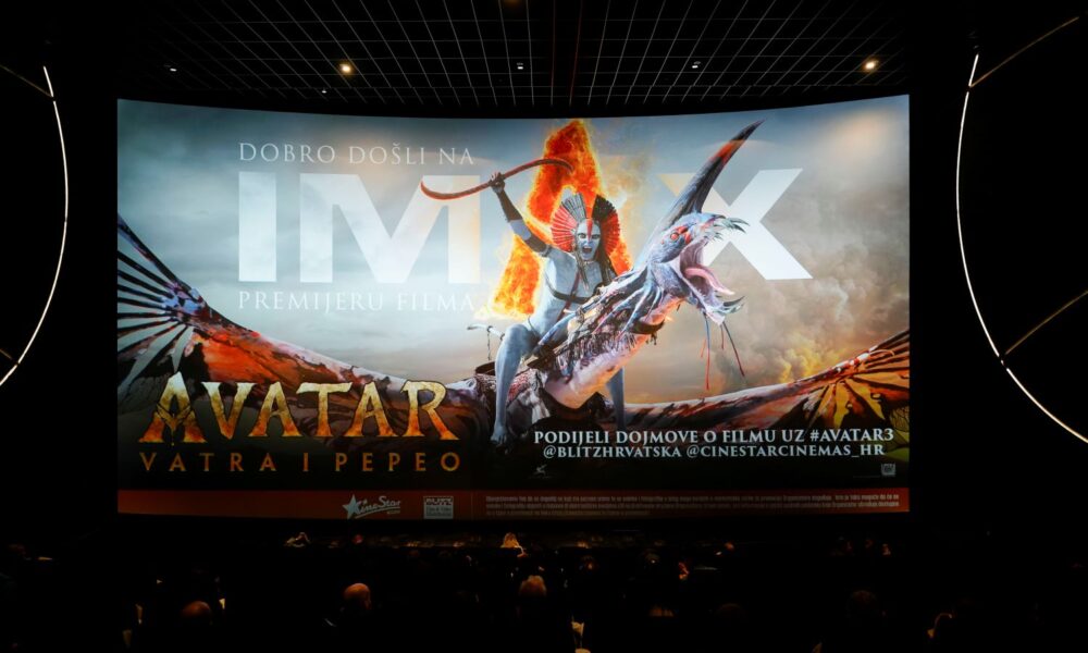 Fotografija prikazuje IMAX kino dvoranu tijekom premijere filma „Avatar: Vatra i Pepeo”. Na velikom kino platnu dominira promotivni plakat filma s dramatičnim prizorom: lik jaše leteće stvorenje, drži oružje i okružen je plamenom, što stvara snažan vizualni dojam akcije i fantazije. U dvorani su gledatelji već smješteni i gledaju prema platnu, što dodatno naglašava atmosferu iščekivanja i uzbuđenja. Na ekranu se nalazi i tekstualna dobrodošlica: „Dobro došli na IMAX premijeru filma Avatar: Vatra i Pepeo”, uz poziv da se dojmovi podijele na društvenim mrežama s oznakom #AVATAR3 te oznakama @BLITZHRVATSKA i @CINESTARCINEMAS_HR. U donjem dijelu ekrana istaknuti su logotipi CineStara i Blitz-a, a prisutna je i napomena da je kino opremljeno kamerama za snimanje i fotografiranje u promotivne svrhe, uz obavijest da ulaskom u prostor korisnici pristaju na takvo dokumentiranje.