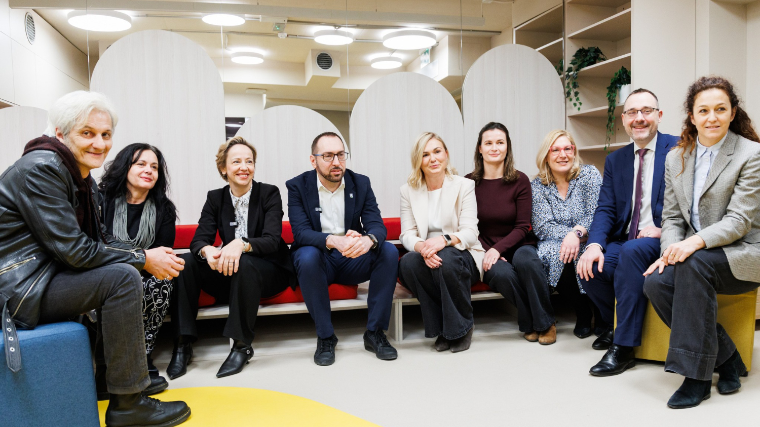 Devet osoba sjedi u polukrugu u moderno uređenom interijeru, među njima i zagrebački gradonačelnik Tomislav Tomašević. Svi su opušteni i nasmijani, a prostorija ima tople tonove, dizajnerski namještaj i police s biljkama.