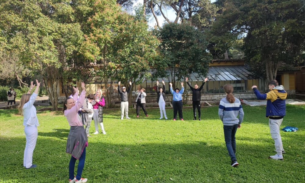 Fotografija prikazuje nekoliko ljudi kako se druže na livadi.