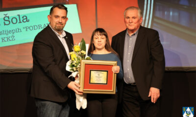 Dodjela priznanja: žena prima nagradu i cvijeće uz dva predstavnika na pozornici.