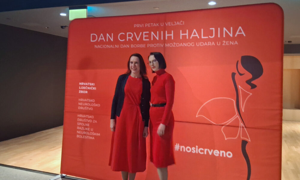 Dvije žene u crvenim haljinama poziraju ispred službenog crvenog panoa s natpisom “Dan crvenih haljina – Nacionalni dan borbe protiv moždanog udara u žena”. Na pano su istaknuti organizatori, uključujući Hrvatski liječnički zbor i Hrvatsko neurološko društvo.