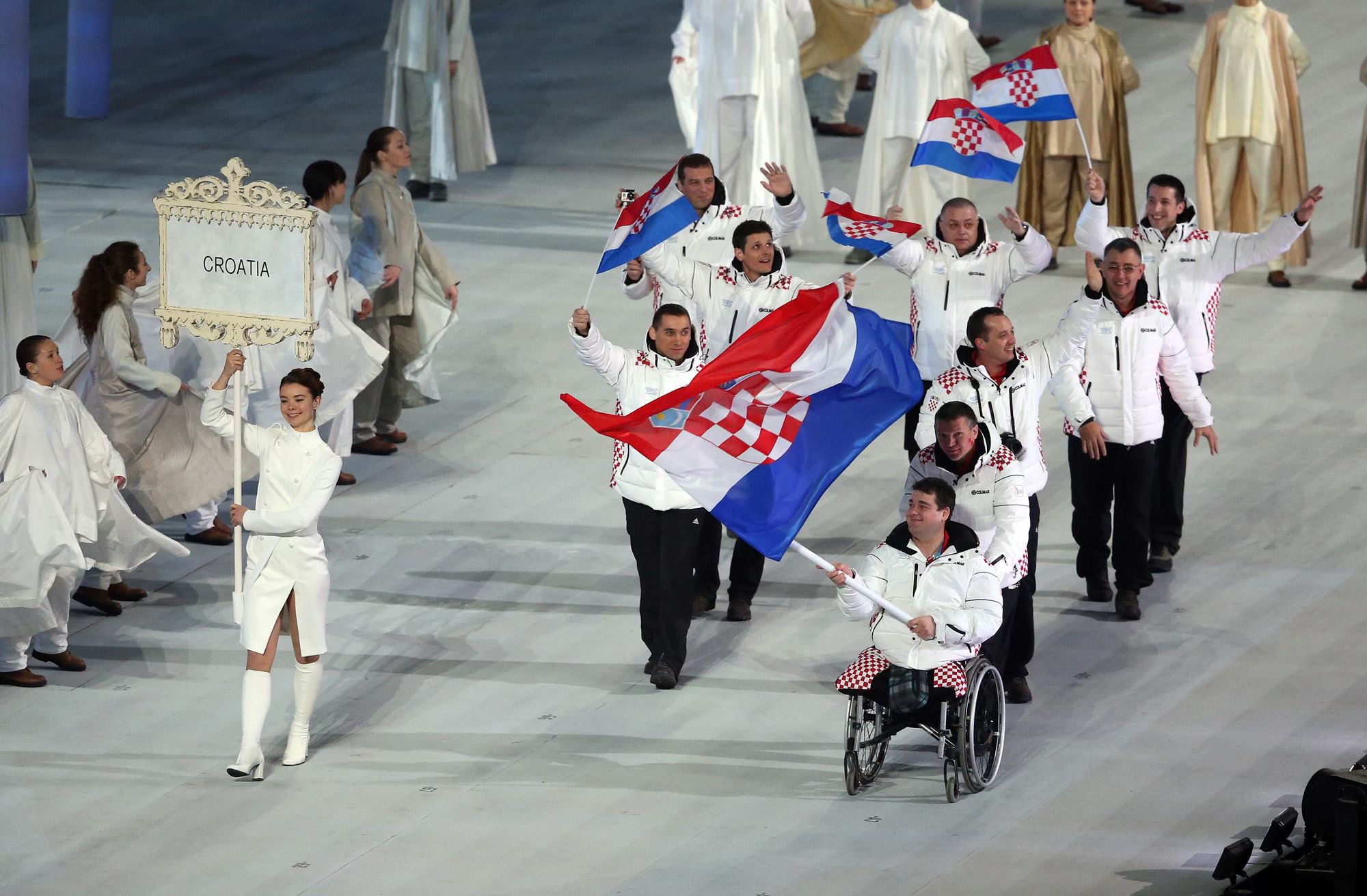 Fotografija prikazuje više ljudi na ceremoniji, a jedan čovjek bez nogu u kolicima nosi hrvatsku zastavu.