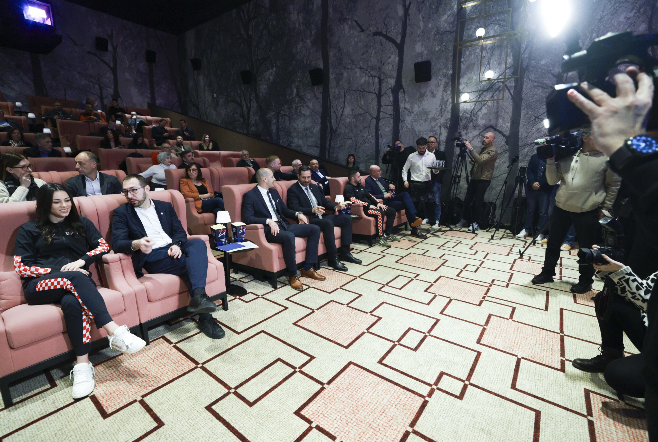Publika i uzvanici u kinu; novinari i kamere snimaju događanje u dvorani.