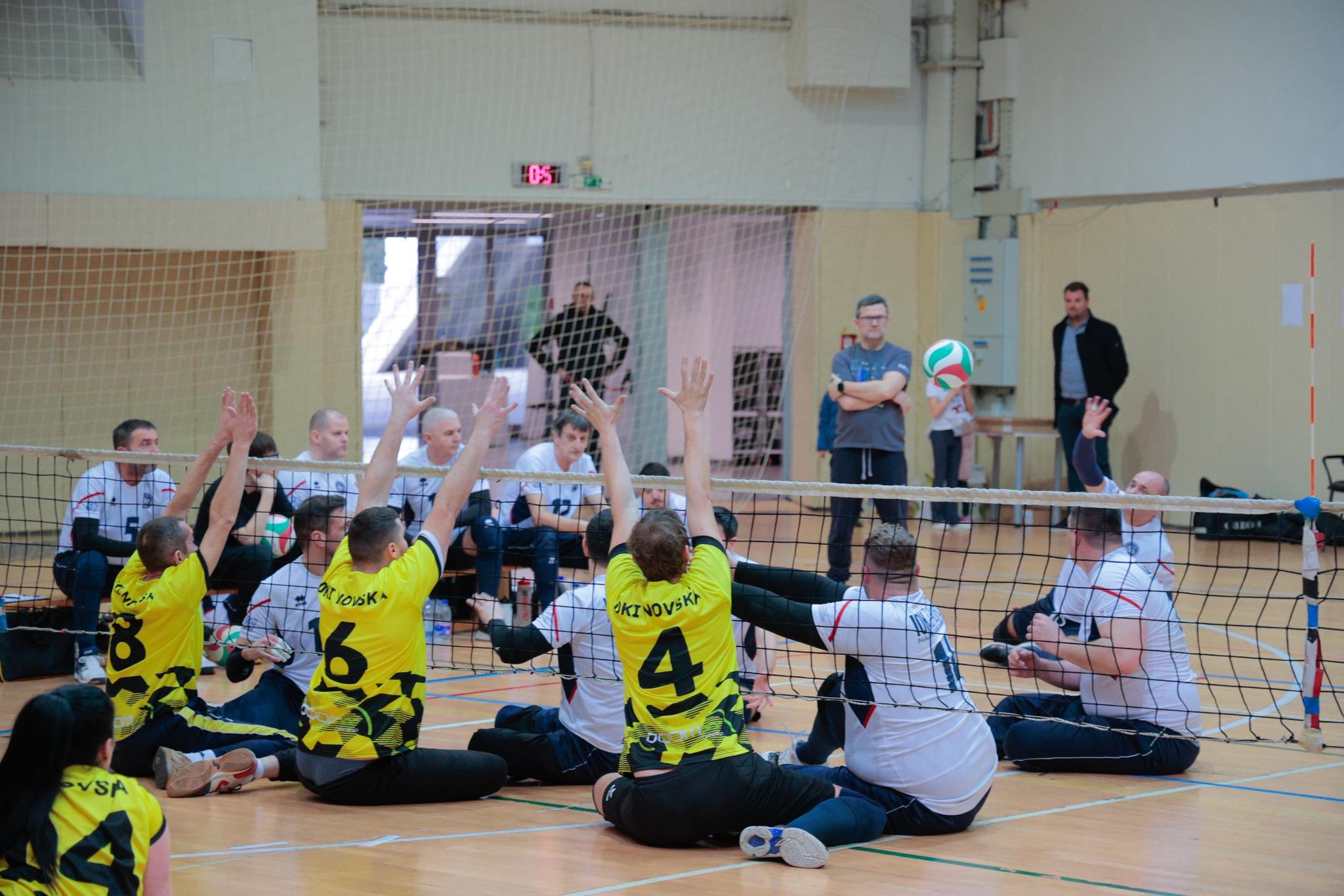 Na fotografiji su prikazani igrači sjedeće odbojke koji igraju utakmicu u dvorani.